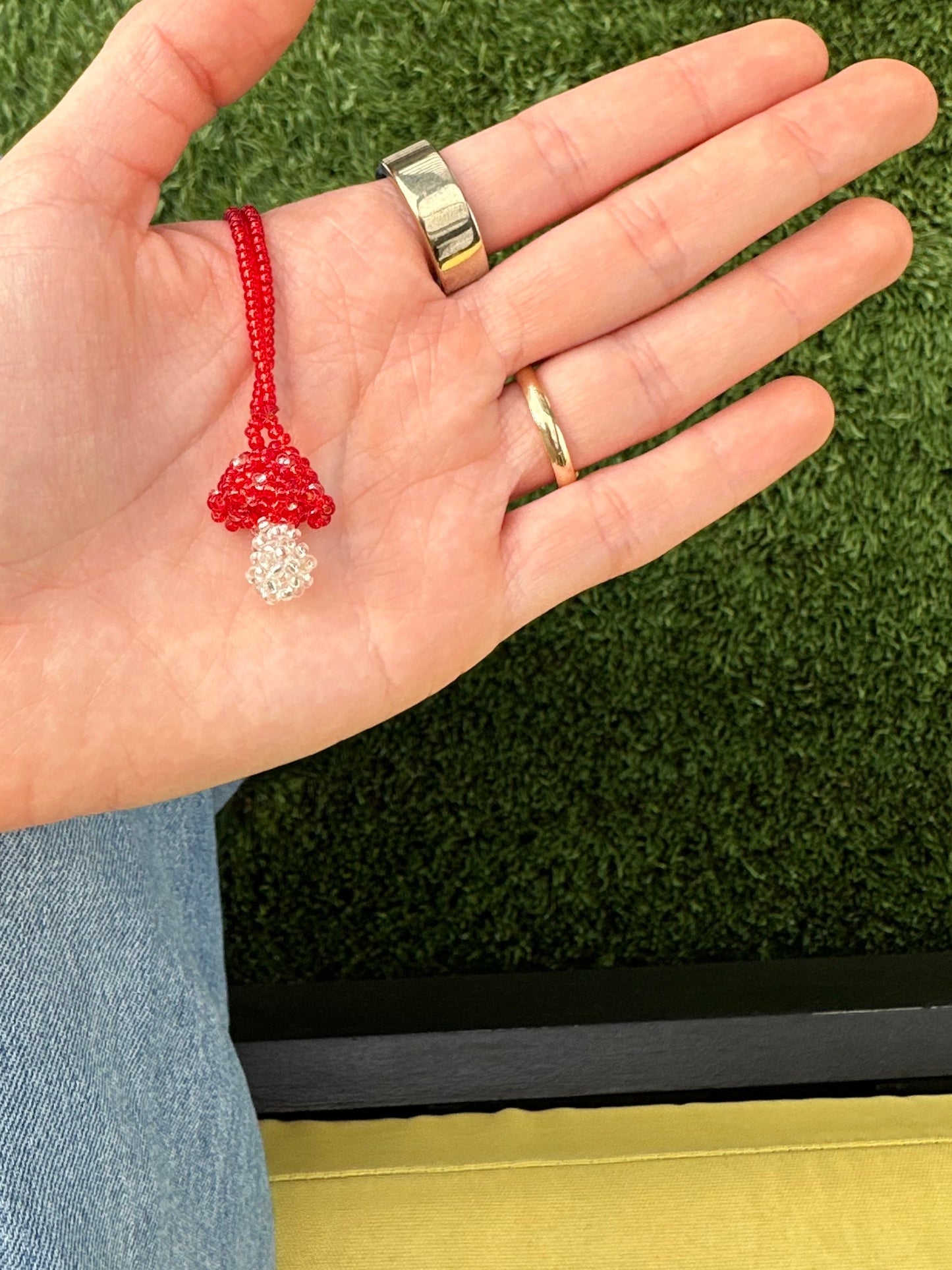 Hand holding a red string bracelet with grass in the background