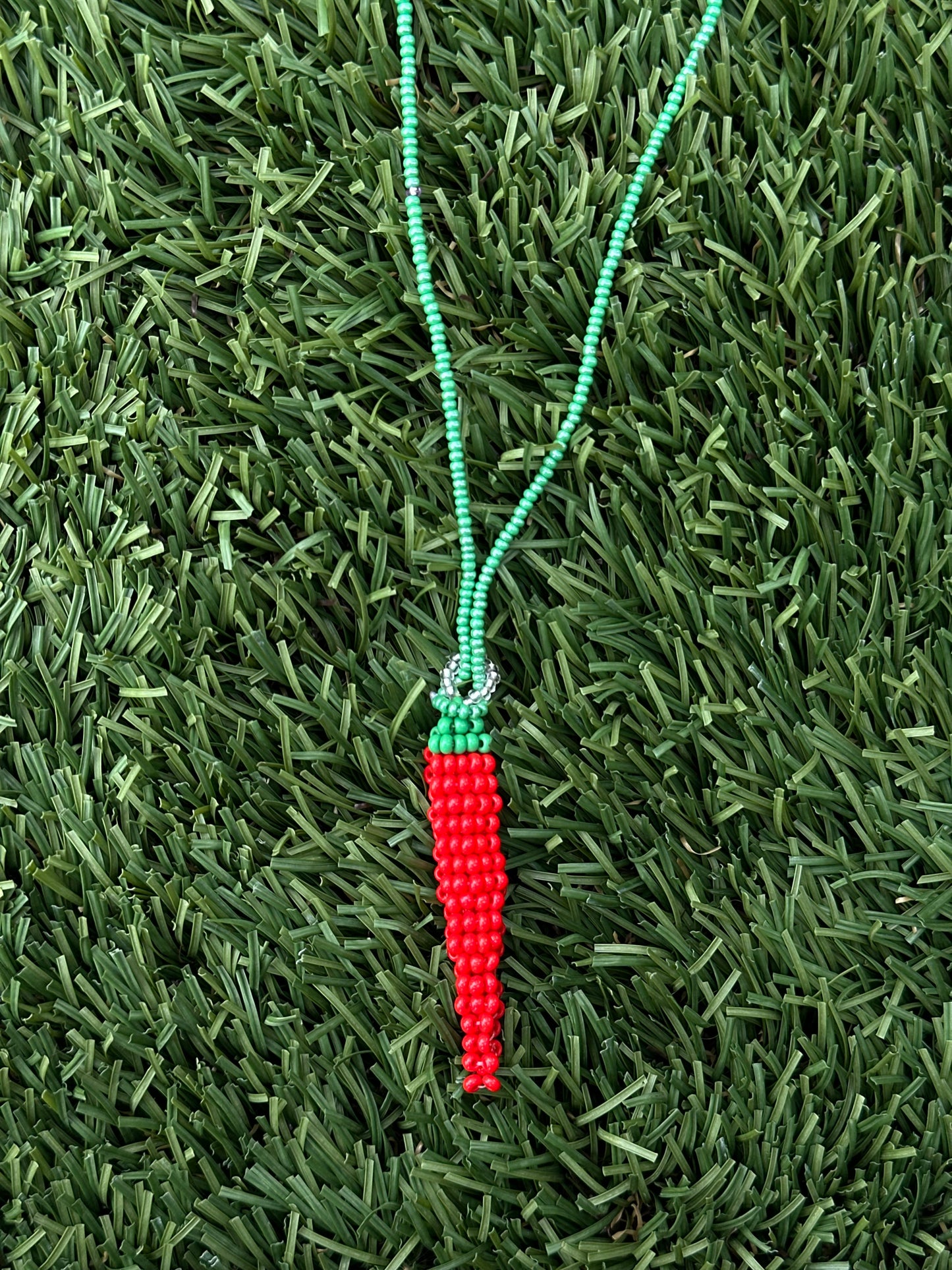 Pepper-shaped beaded charm on a green string against a grassy background