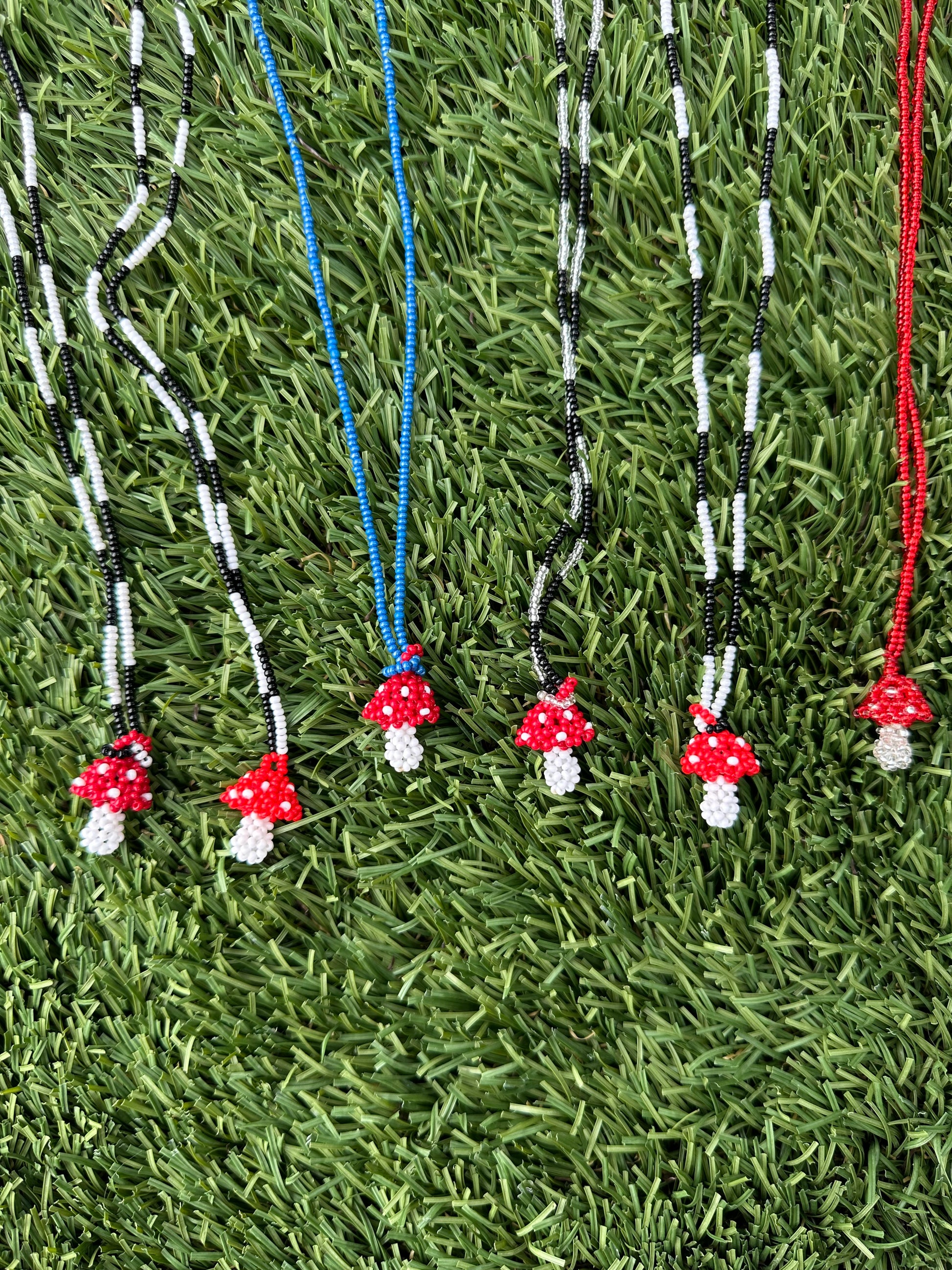 Red mushroom-shaped charms on black and white beaded strings against a green grass background